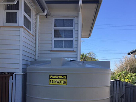 Residential rainwater tank and downpipe connection beside a weatherboard house
